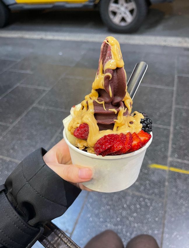 Wing Pang holding an açai bowl in a cup with peanut sauce and fruits.